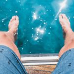 young man's knees next to sparkling swimming pool
