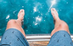 young man's knees next to sparkling swimming pool